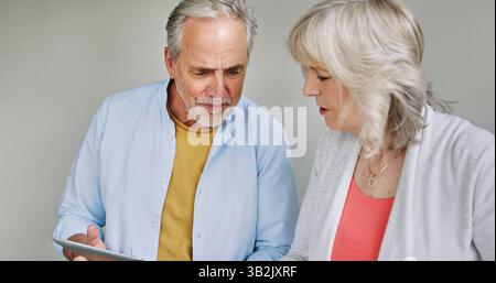 Tablet, information and senior couple talking together in studio on white background for research. Technology, thinking or online crossword with an Stock Photo