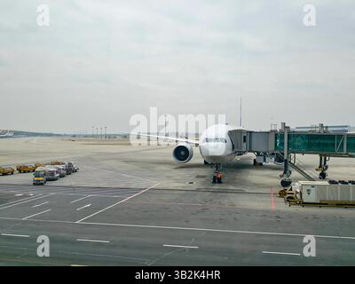 Large passenger jet parked at Beijing Capital International Airport, with a jet bridge attached and a service crew working on the front chassis. Stock Photo