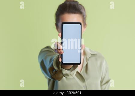 A woman with a bun holds a smartphone with a blank screen, obscuring her face. Ideal for mobile app promotions and anonymous tech use. Stock Photo