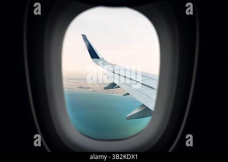 View of airplane wings in clouds through porthole. Blue sky background. Beautiful clouds and airplane wings from the window with beautiful blue sky Stock Photo