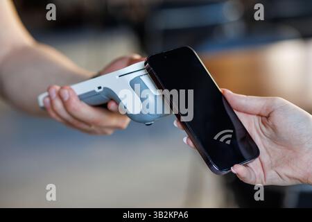 Close-up of a customer making contactless payment using smartphone and NFC technology at a store checkout. Stock Photo