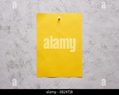 Blank yellow sheet of paper pinned to a white concrete wall. Stock Photo