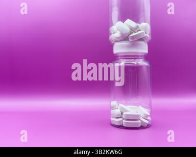Two transparent jars with white pills, on a pink background, front view. Stock Photo