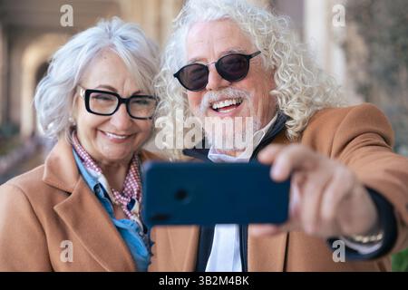 Caucasian senior couple smiling and taking selfie with smartphone outdoors Stock Photo