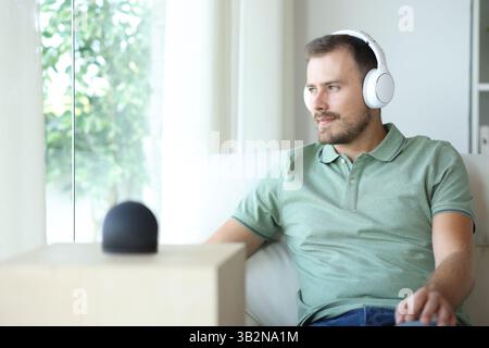 Happy man listening music with headphone from smart speaker sitting on a couch at home Stock Photo