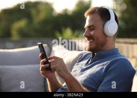 Happy man wearing headphones in a terrace listening audio using phone Stock Photo