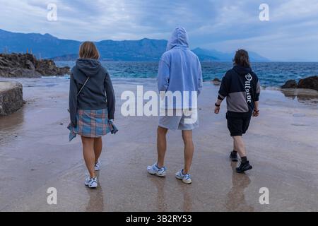 Three people in hoodies walking on wet pier by the sea Stock Photo