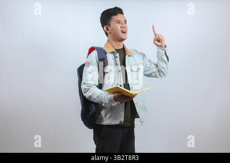 Asian man wearing denim jacket carrying books and bag showing finger up having brilliant idea isolated on white background,education concept Stock Photo