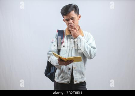 university student wearing denim jacket carrying bag and reading book seriously isolated on white background Stock Photo