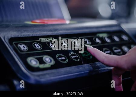 A person's finger presses the start button on a treadmill, initiating a workout session. The image emphasizes the act of starting exercise and fitness Stock Photo
