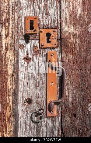 Rusty handle and keyholes in weathered timber door - France. Stock Photo