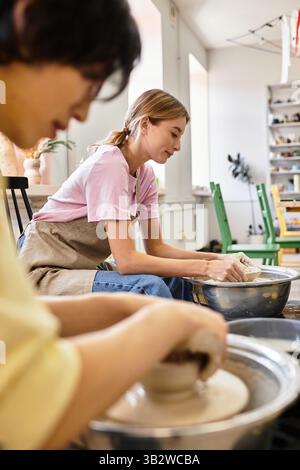 A young couple happily shapes clay on pottery wheels in their studio. Stock Photo
