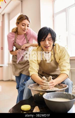A couple joyfully makes pottery together, showcasing their love in a bright studio. Stock Photo
