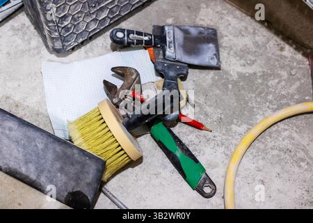 A collection of various tools scattered on the ground, which includes a wrench, a brush, and other useful items for different tasks Stock Photo