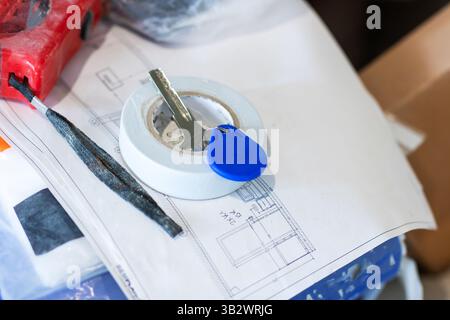 A single key is resting on a piece of white paper located right next to a distinct blue plastic tag, creating an interesting visual contrast Stock Photo