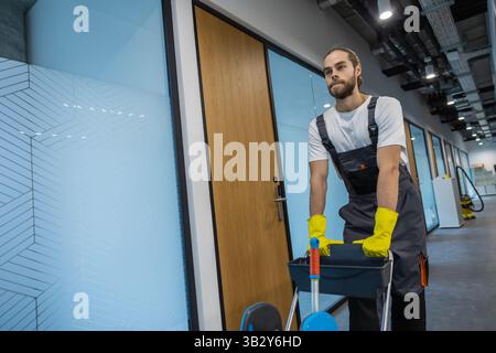 Young man in uniform walking in the office corridor and pushing the cart Stock Photo