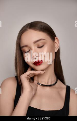 young model showcases bold red lips and a sleek hairstyle while posing confidently in a minimalist studio. Stock Photo