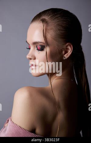 model stands gracefully with her back to the camera, showcasing bold makeup and sleek hair in a studio setting. Stock Photo