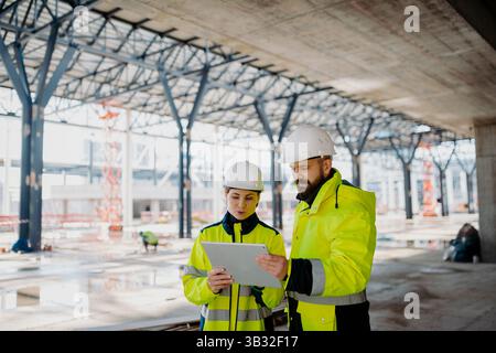 Engineers discussing construction plans using a tablet on site. Stock Photo