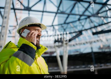 Construction site manager making phone call while inspecting building site. Stock Photo