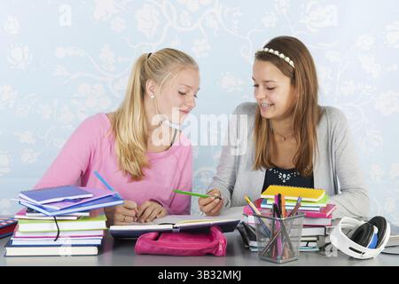 Two teengirls sitting at desk making homework together Stock Photo