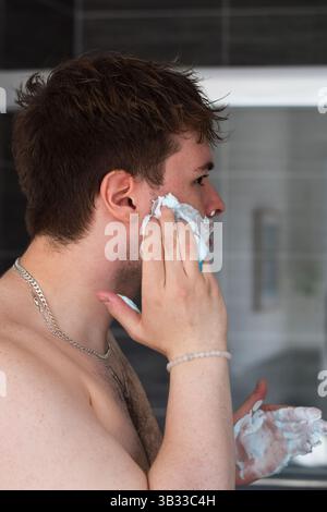 Young man shaving in front of mirror in the bathroom Stock Photo