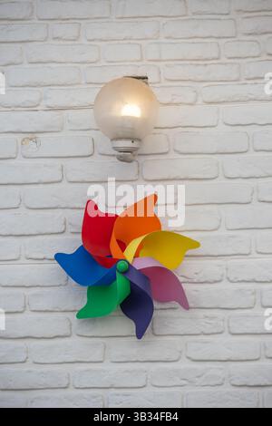 A rainbow pinwheel adds a vibrant pop of color to a simple white wall, sitting directly under a softly lit, globe Stock Photo