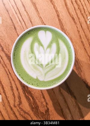 Top view of a cup of matcha latte with beautiful green and white latte art on a wooden table, perfect for themes of healthy drinks, cafe culture, cozy Stock Photo