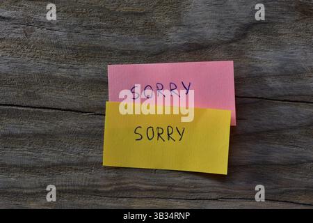 Message sorry on pink and yellow sticky notes on wooden board textured background. A pen wrote word sorry on note papers. Stock Photo
