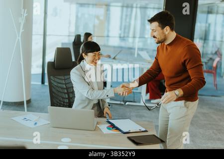 Bright office environment sees a joyful handshake between a male and female professional. They exchange smiles, indicating a fruitful collaboration af Stock Photo