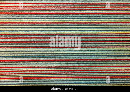 Colorful striped carpet texture with red, yellow, blue and gray lines creating abstract pattern. Stock Photo