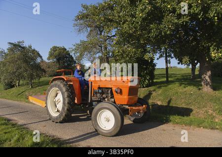 Farm boys with chickens riding on orange tractor Stock Photo - Alamy