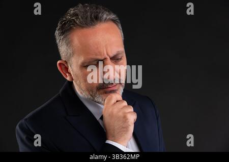 Serious mature businessman in suit shown in close-up, reflecting deeply with hand on chin, symbolizing decision-making and analysis. Stock Photo