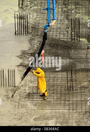 Construction worker managing concrete flow from pump during foundation work at a building site. Manual labor in the construction industry. Stock Photo