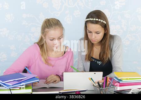Two teengirls sitting at desk making homework together using a digital tablet Stock Photo