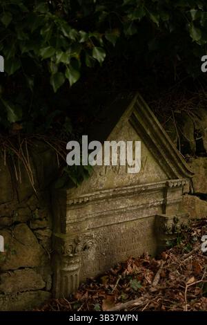Old stone gravestone partially covered by moss, in a quiet overgrown ...