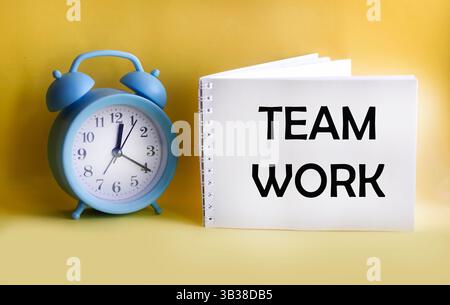 The word "TEAMWORK" is written on a notepad and a yellow background, and the clock is nearby. Stock Photo