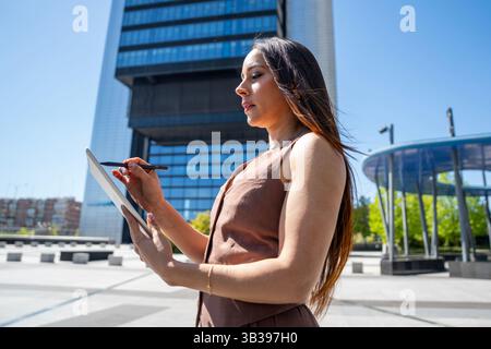 Businesswoman using digital tablet and stylus pen for work outdoors in modern business district Stock Photo