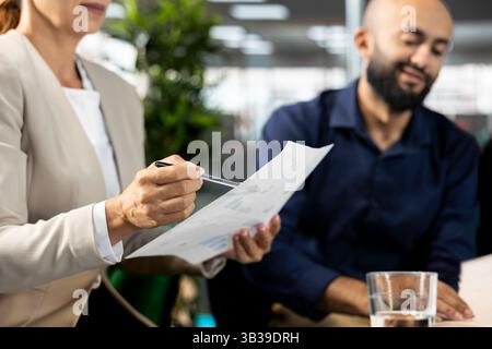 Multiracial coworkers doing briefing meeting to share new ideas for profit growth, presenting files. Team of workers in office talking with supervisor, showing project documentation Stock Photo