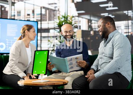 Green screen device next to smiling colleagues doing brainstorming, coordinating company administrative operation. Close up of mockup tablet used by joyous team of office clerks reviewing data Stock Photo