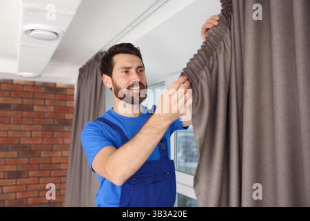 Worker in uniform hanging window curtain indoors Stock Photo
