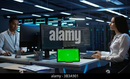 Data center developer responsible for installation of networking equipment solving tasks on green screen device. Woman doing maintenance on server room infrastructure using chroma key tablet, camera B Stock Photo
