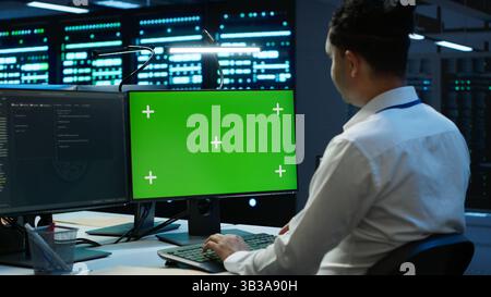 Programmer in data center managing and maintaining databases using mockup PC, ensuring data integrity and security. Expert updating server room systems using green screen computer, camera A Stock Photo