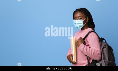 Education During Pandemic. Black Female Student In Protective Mask On Purple Background Stock Photo