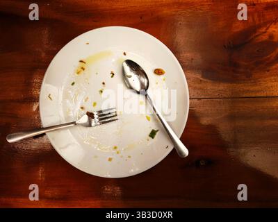 White plate with spoon and fork after use for eating on wooden table Stock Photo