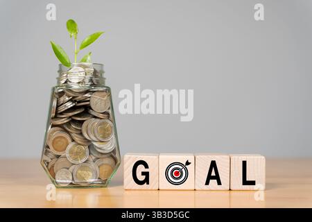 A glass bottle filled with coins and wooden blocks and the word GOAL symbolizes financial growth and future planning. Achievement goals set. Stock Photo