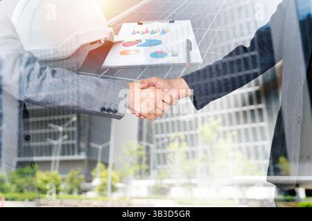 Business professionals shaking hands over solar panels reflecting a commitment to renewable energy and sustainable development in an eco-friendly part Stock Photo