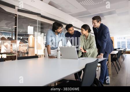 Four multiethnic professionals gathered around laptop in corporate office Stock Photo