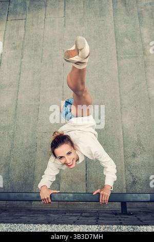 a ballerina shows stretching doing vertical splits on street stairs while walking around the city Stock Photo
