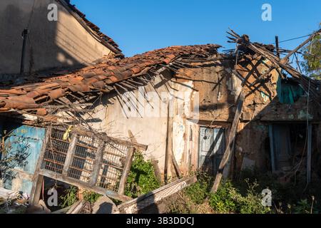 An old, ruined, rustic house with a thatched roof and mud brick walls in a village in South India. Stock Photo